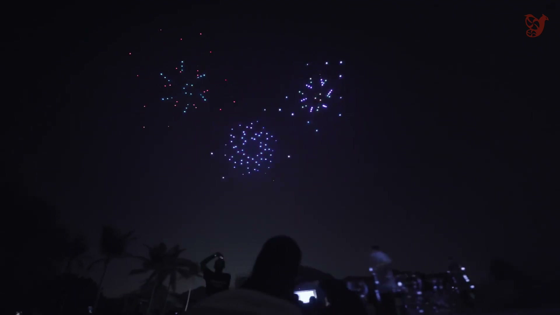 Drones draw bursts of light in the night sky above the audience
